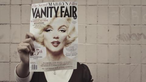 A person holding a magazine cover featuring Marilyn Monroe's face over her own face, suggesting an AI deepfake