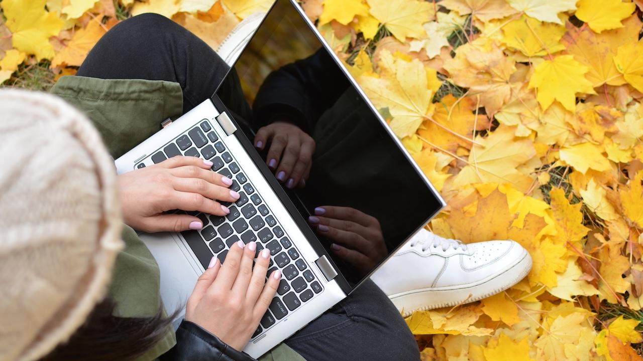 Woman with laptop among fallen yellow leaves